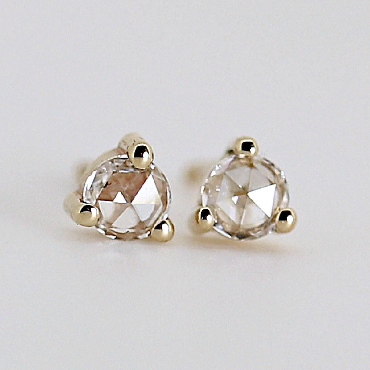 Two small gold stud earrings with faceted round stones resting on a light surface.
