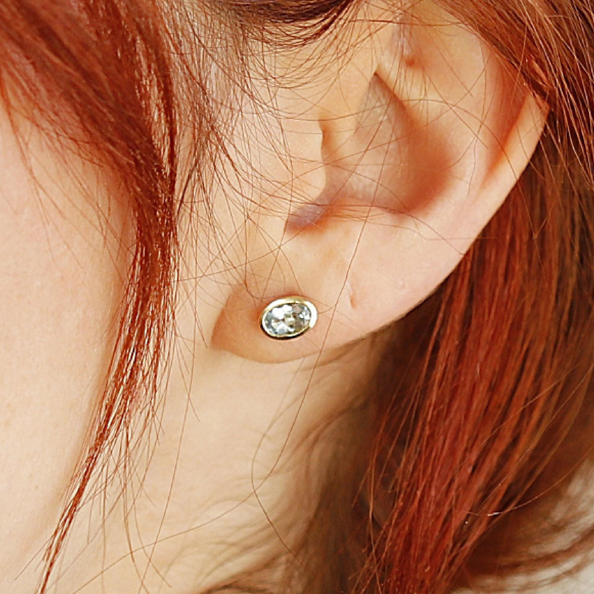 Close-up of a single oval light blue gemstone bezel-set in gold worn on an earlobe.