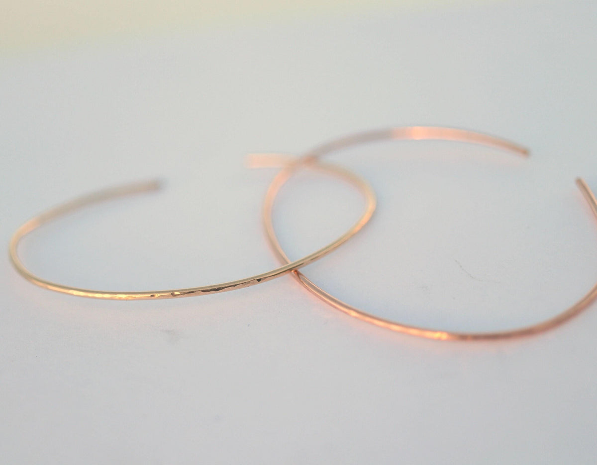 Two thin rose gold hammered cuff bracelets lie flat on a neutral white surface.