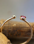 Close-up view of the gold open ring resting on wood, showing the gap between the bezel-set ruby and the terminal gold ball.
