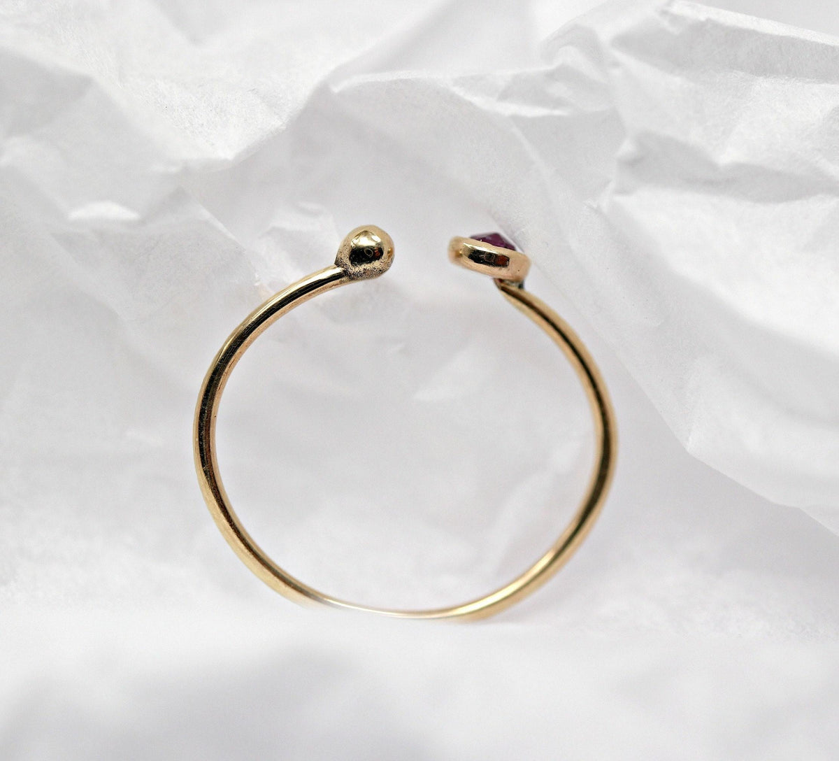 Back view of the curved gold open ring displayed against white crumpled paper.