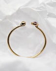 Back view of the curved gold open ring displayed against white crumpled paper.