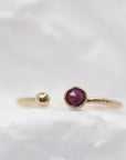 Close-up of the gold ring with a ruby and ball terminal resting on crumpled white paper.