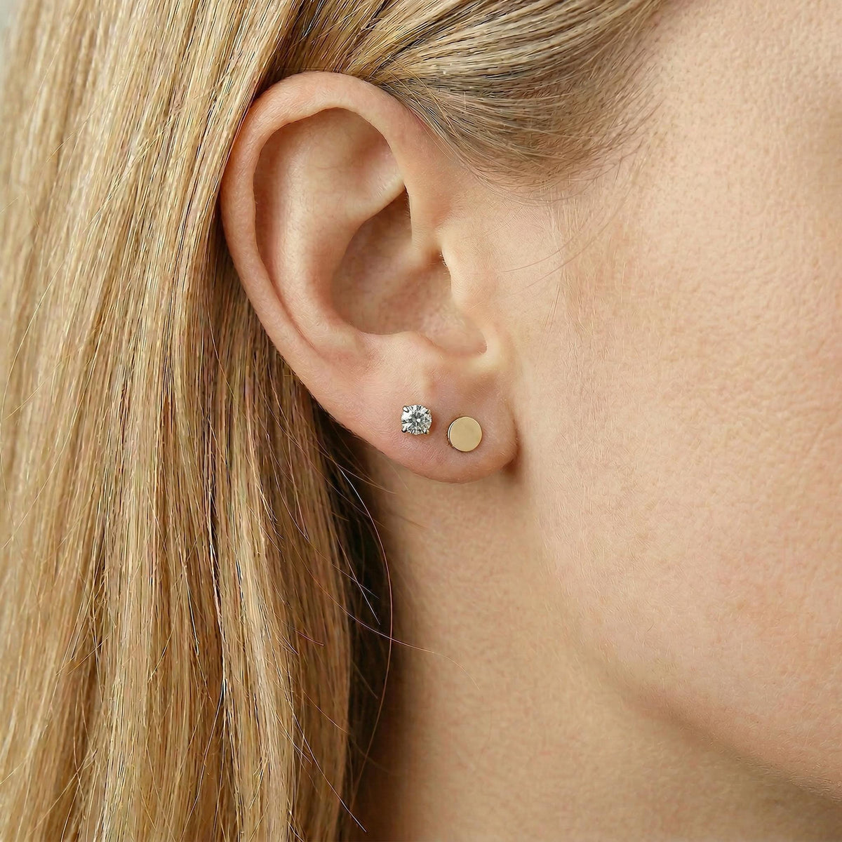 Close-up of a person's earlobe wearing a round diamond stud earring and a flat gold circle stud earring.