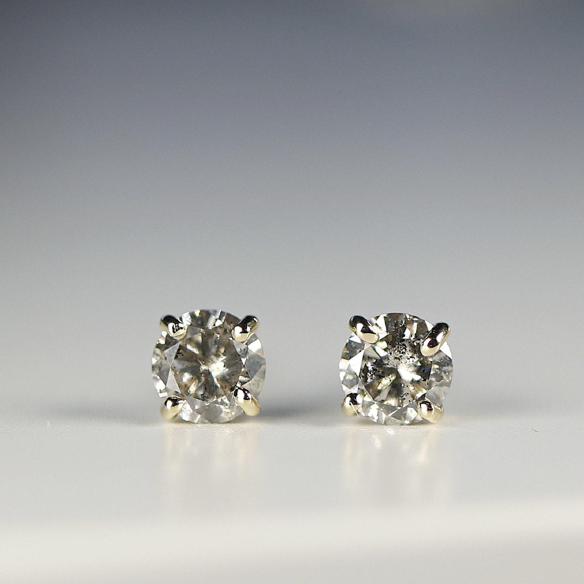 Front view of two speckled gray diamond earrings set in gold prongs on a pale background.