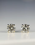 Front view of two speckled gray diamond earrings set in gold prongs on a pale background.
