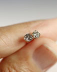 Two speckled grey diamond stud earrings held gently on the tip of a finger.