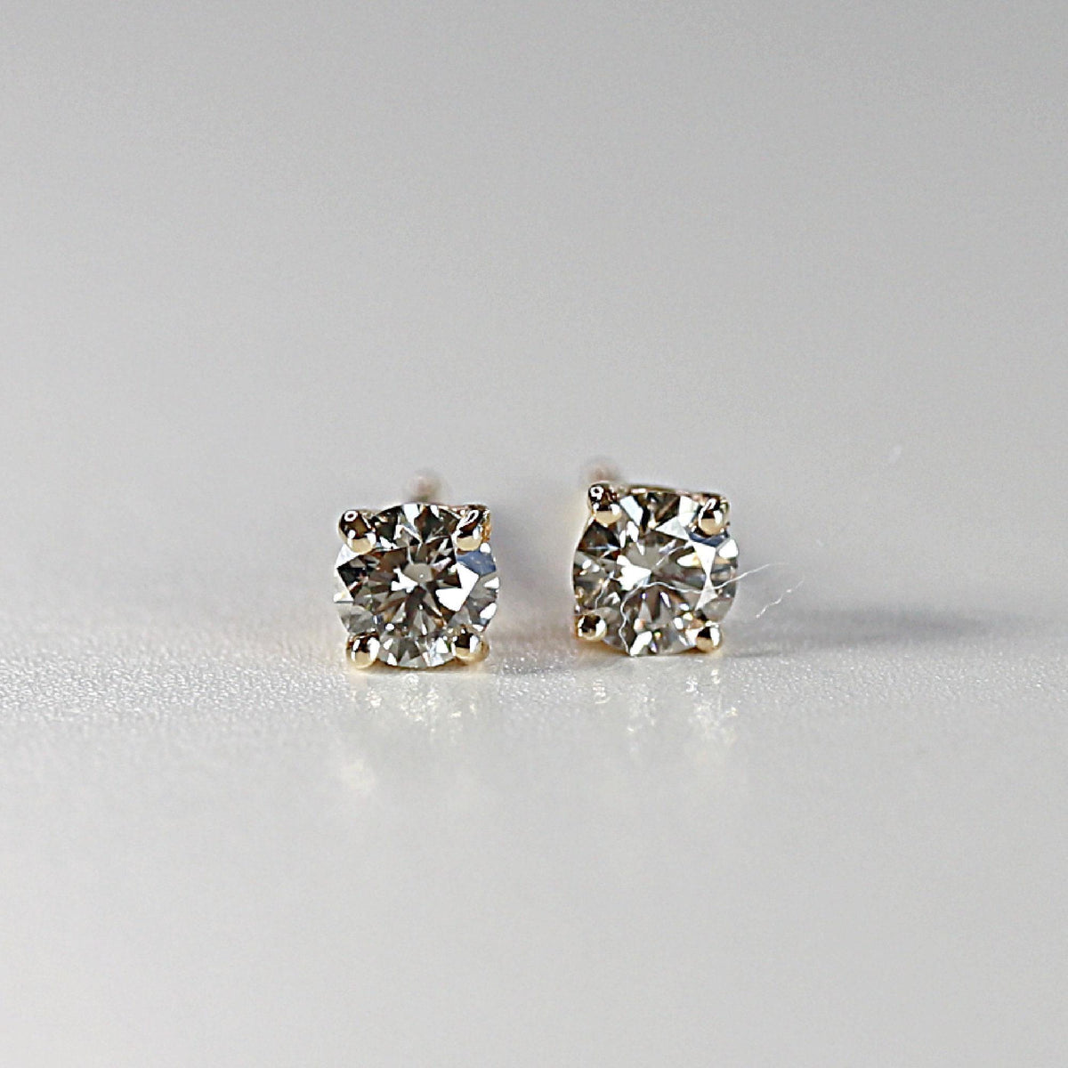Close-up of two sparkling salt and pepper diamond stud earrings in gold prongs against a plain white background.