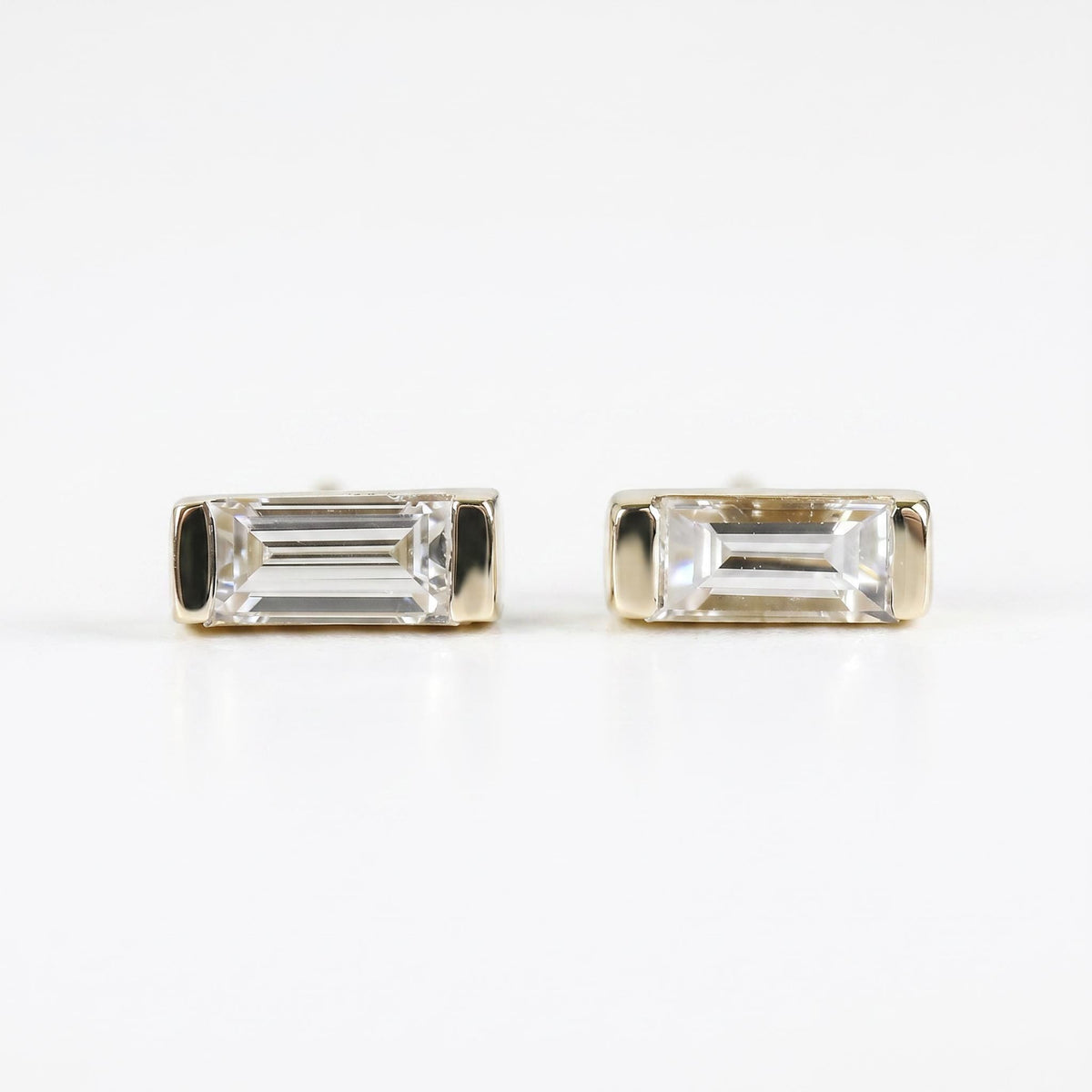 Two gold baguette diamond stud earrings displayed on a white surface.
