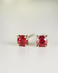 Close-up front view of two round red gemstone stud earrings in gold settings on a flat white surface.