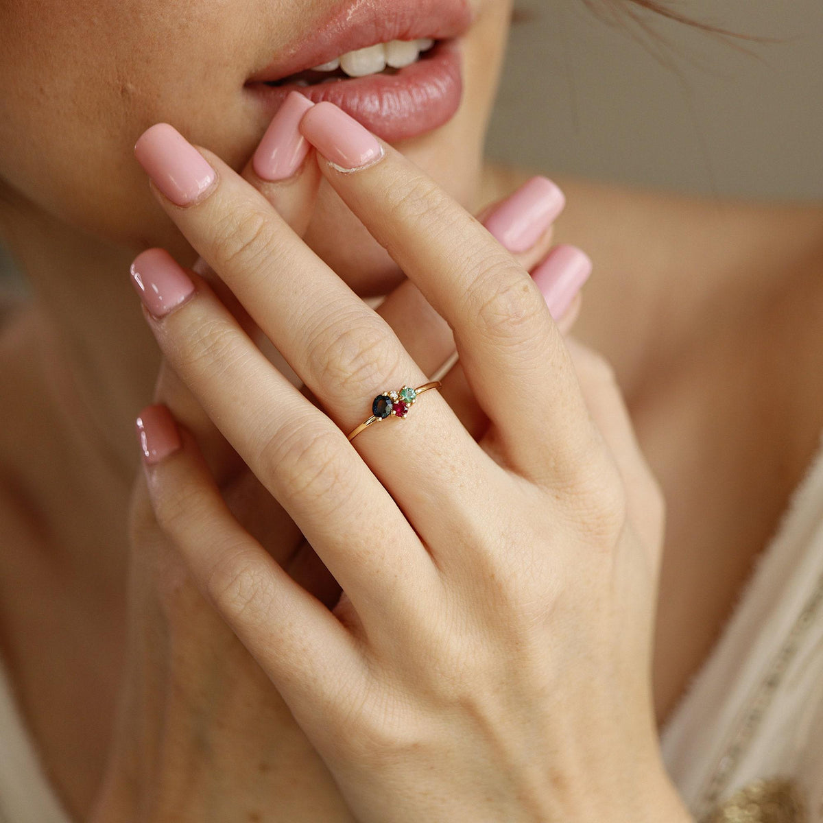 Close-up of a person wearing the gold multi-gemstone cluster ring on their ring finger, with light pink polished fingernails.