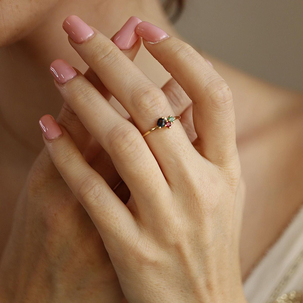 A hand wearing the gold gemstone cluster ring near the face, showing manicured pink nails.
