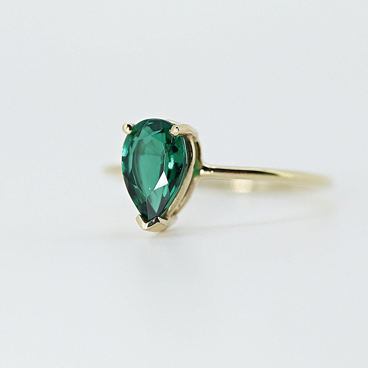 A gold ring with a pear-cut green gemstone set in a four-prong setting, viewed from an angle against a white background.