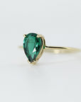 A gold ring with a pear-cut green gemstone set in a four-prong setting, viewed from an angle against a white background.
