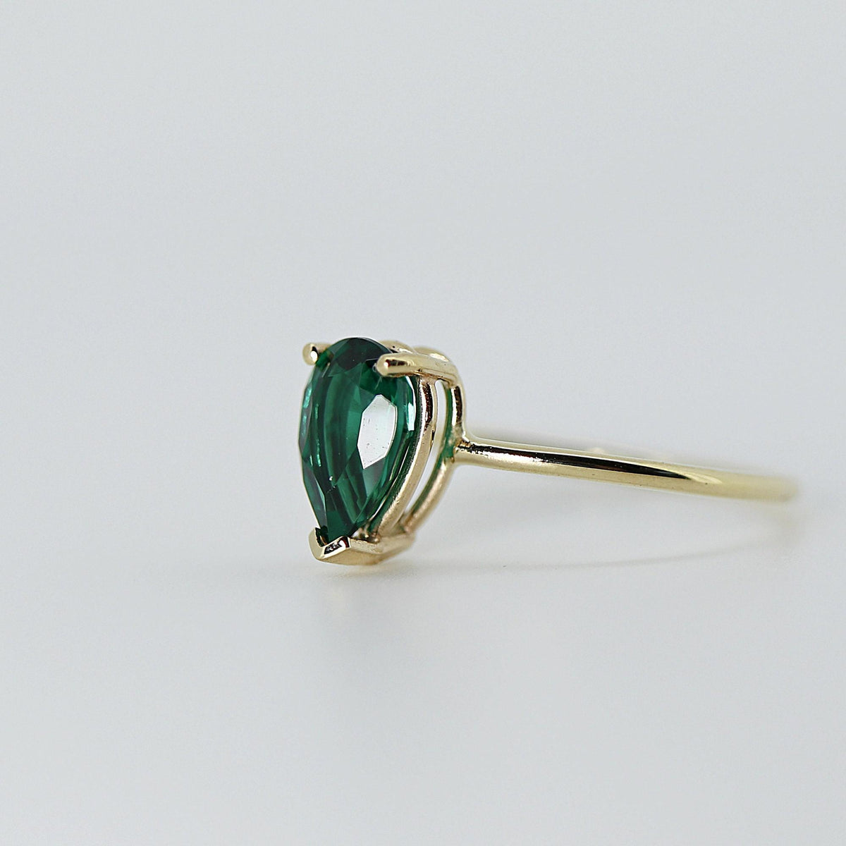 Side-angle view of a gold ring featuring a pear-shaped green stone secured by prongs on a plain gold band.