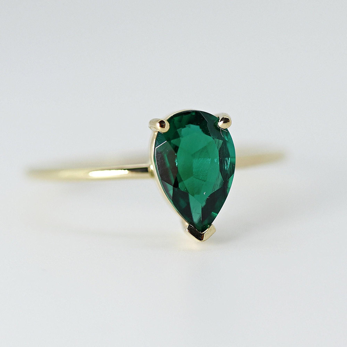 Front view of a faceted pear-cut green emerald set in a yellow gold ring on a clean light background.