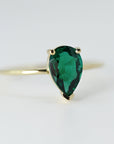Front view of a faceted pear-cut green emerald set in a yellow gold ring on a clean light background.