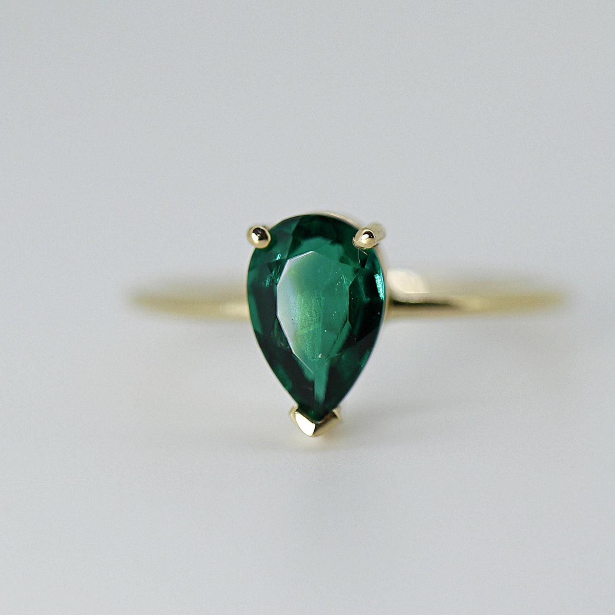 Close-up front shot of the pear-shaped green gemstone in a gold prong setting on a thin band.