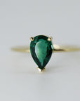 Close-up front shot of the pear-shaped green gemstone in a gold prong setting on a thin band.