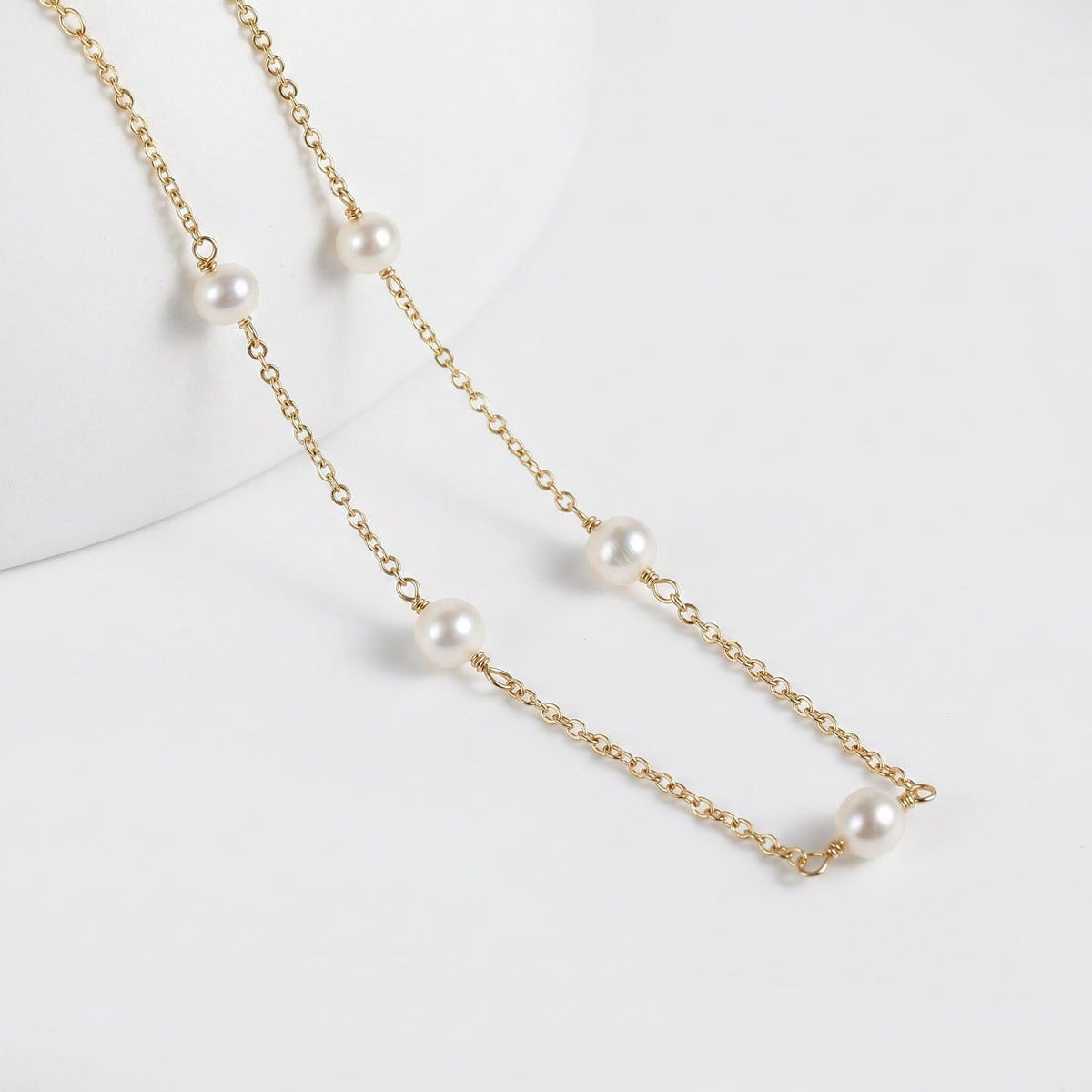 Close-up view of a delicate gold chain necklace featuring small white pearls against a white background.