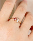 A gold ring with a square pink tourmaline, a marquise opal, and a small round diamond worn on a finger.