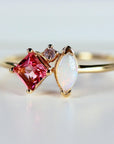 Macro shot of a gold ring showing a square pink tourmaline, marquise opal, and tiny accent stone.