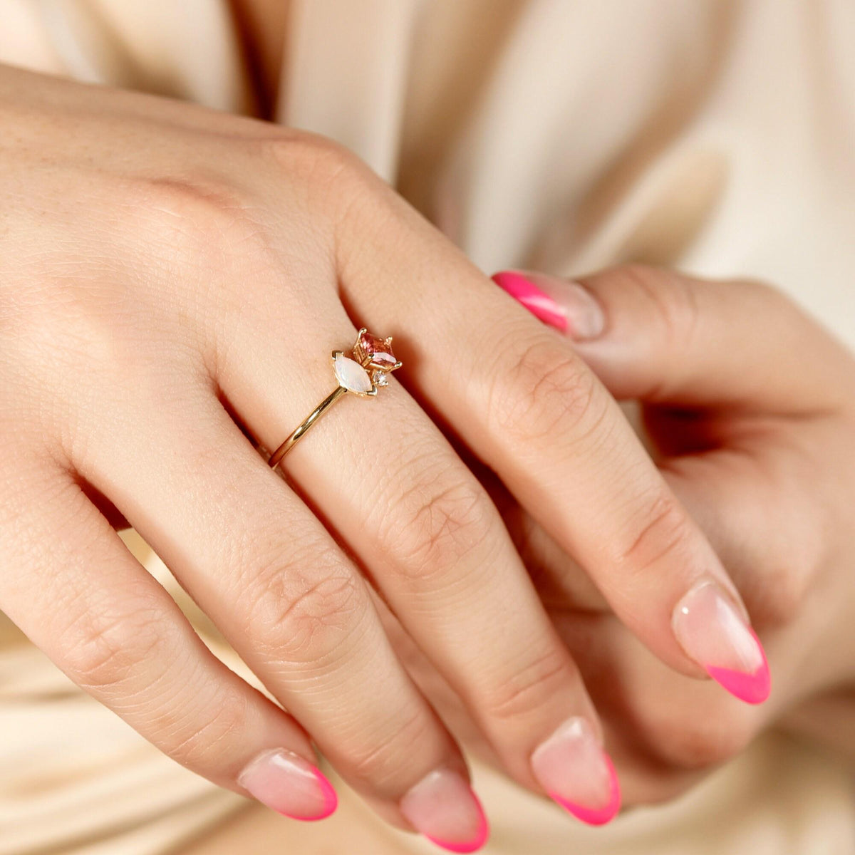 Hand wearing the gold gemstone ring against a beige satin background.
