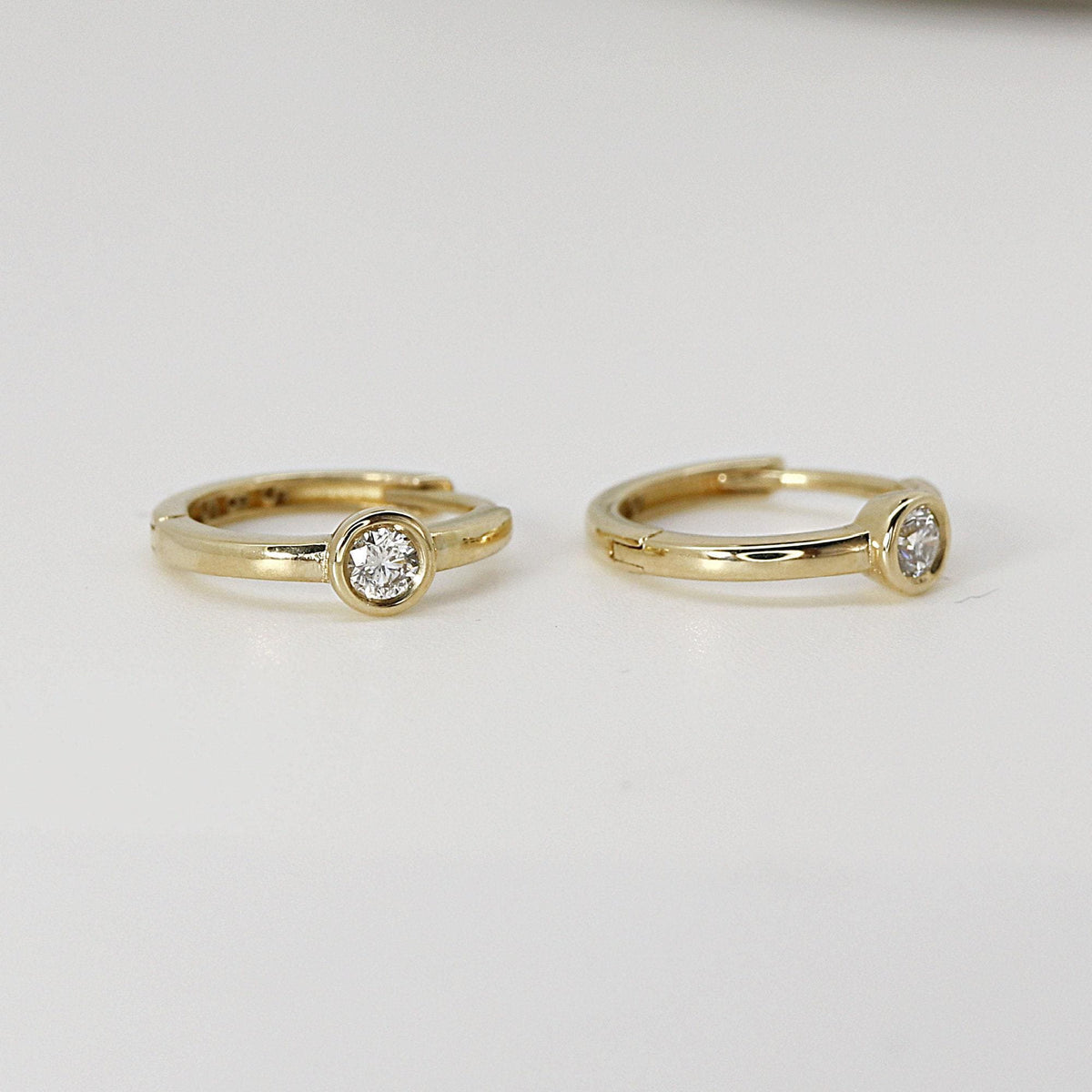 Two gold hoop earrings featuring solitaire diamonds displayed against a plain white background.