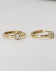 Two gold hoop earrings featuring solitaire diamonds displayed against a plain white background.