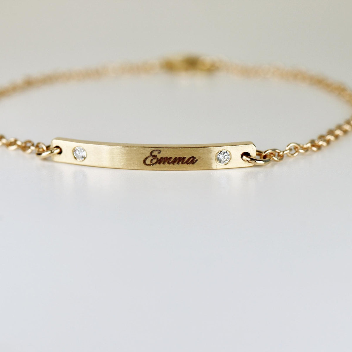 A macro photograph focusing on the engraved name Emma and two flush-set diamonds on a curved gold bar.