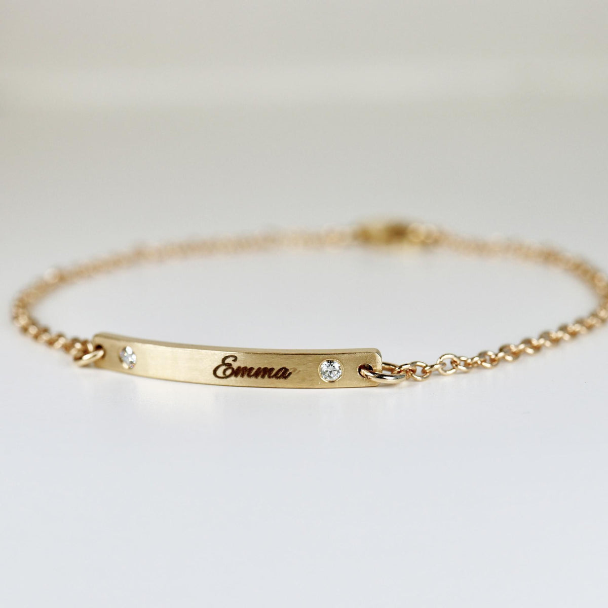 A dainty gold link bracelet rests on a white surface, highlighting its engraved center bar.