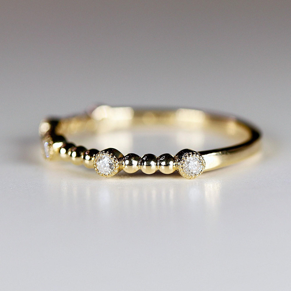 Close-up of a gold ring featuring small round bezel-set diamonds alternating with clusters of gold beads.