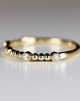 Close-up of a gold ring featuring small round bezel-set diamonds alternating with clusters of gold beads.