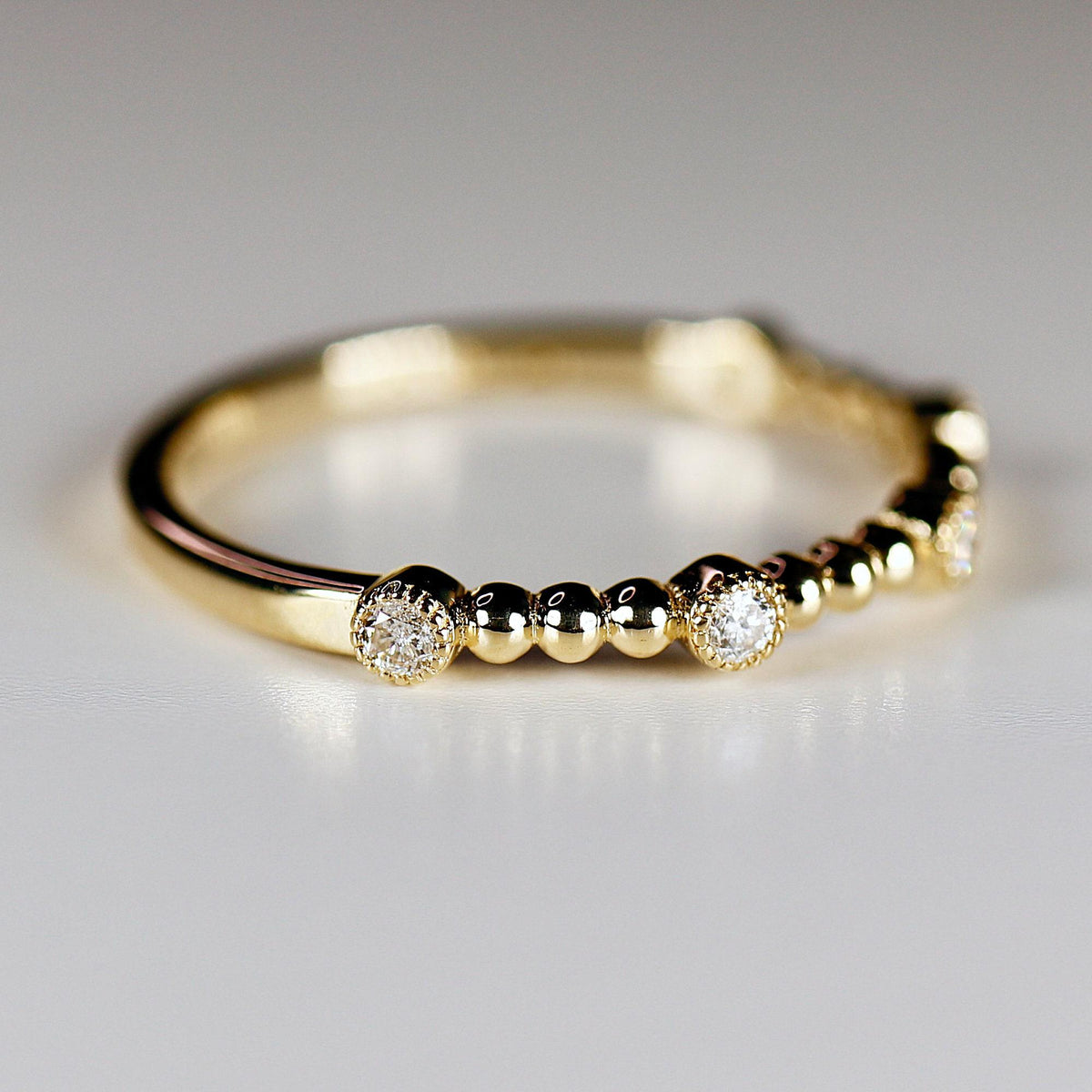 A gold ring with round bezel-set diamonds and alternating small gold beads lying on a light surface.