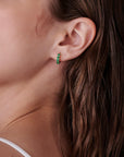 Close-up profile of an ear wearing a small green gemstone huggie hoop earring.