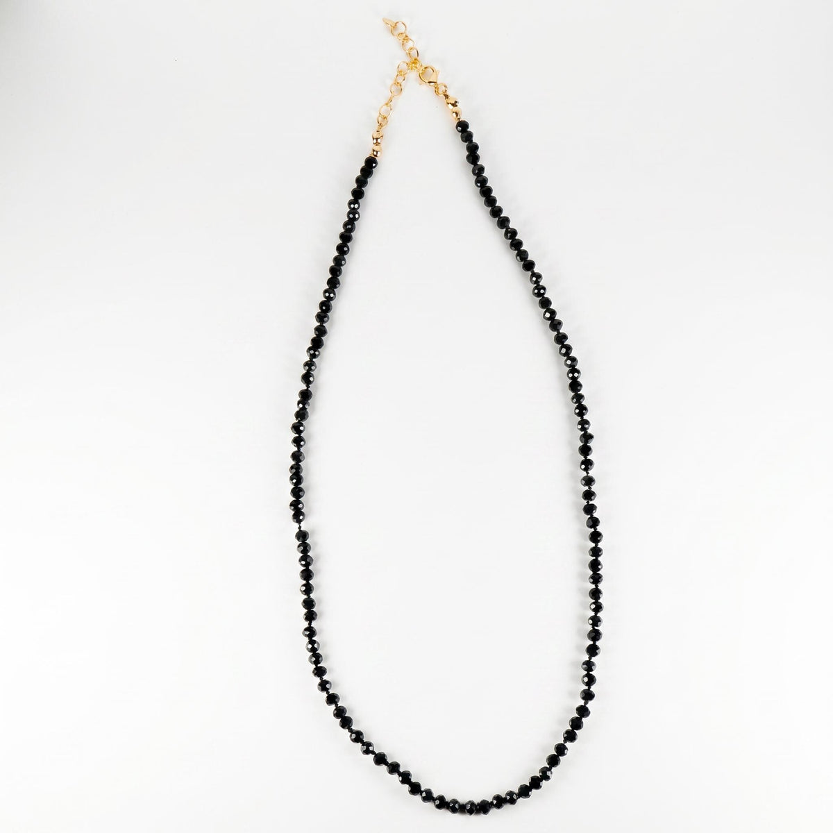 A black spinel bead necklace laid out in a U-shape on a white surface, showing the gold clasp at the top.