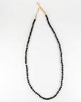 A black spinel bead necklace laid out in a U-shape on a white surface, showing the gold clasp at the top.