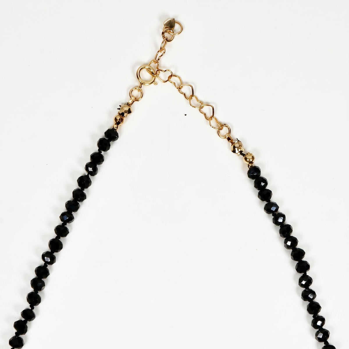 A close-up view of the gold-colored clasp and heart-shaped extender links on a black beaded necklace.