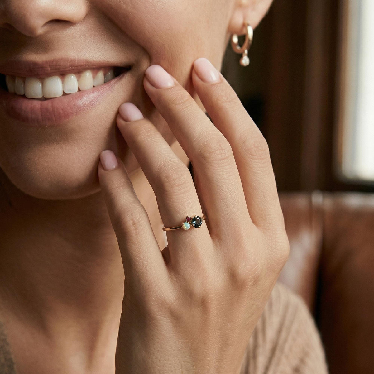 A smiling woman wearing a gold ring with a cluster of three gemstones on her ring finger.