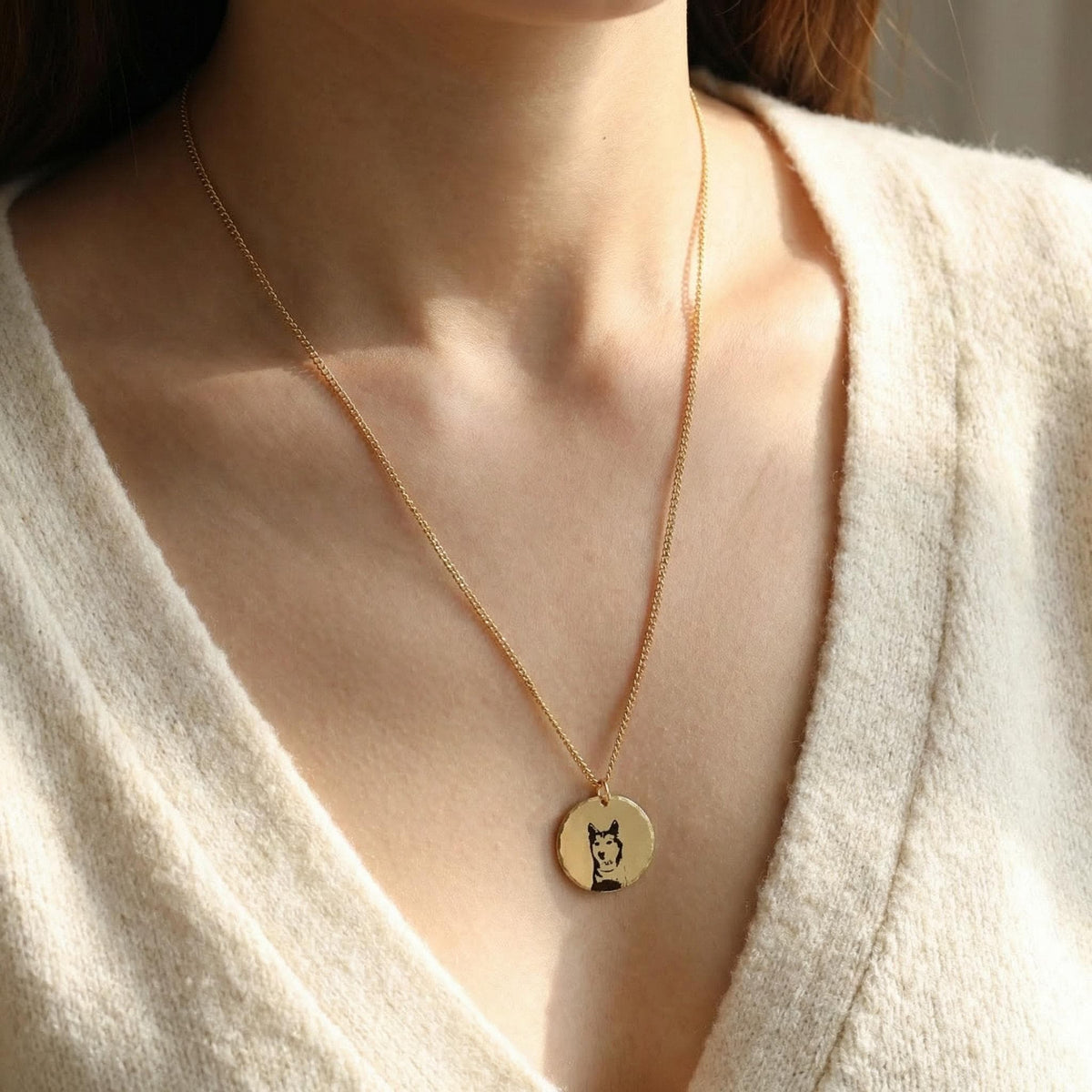 Close-up of a woman wearing a cream sweater and the gold-filled engraved husky coin necklace.