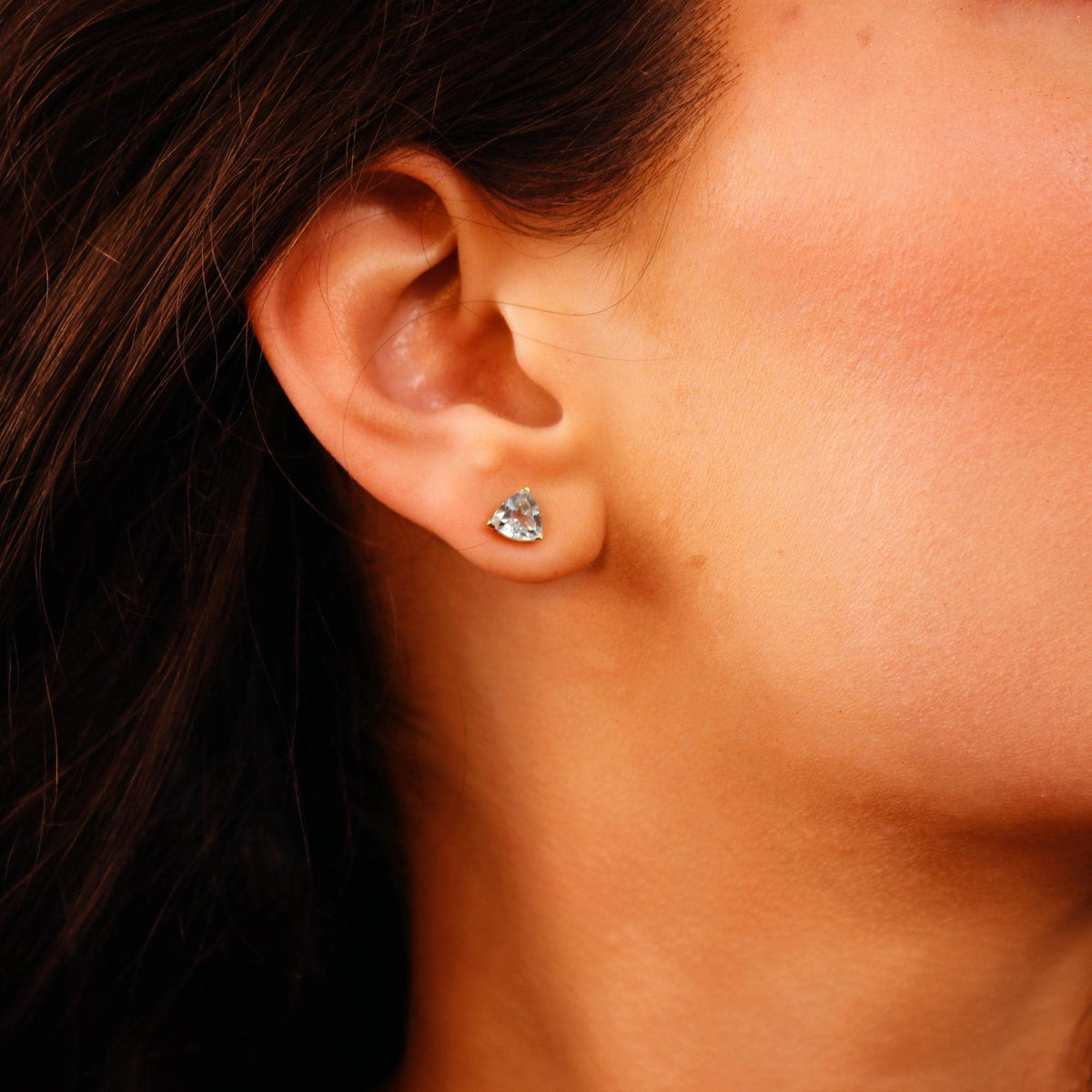 Side view of a person wearing a small triangular gemstone stud earring.