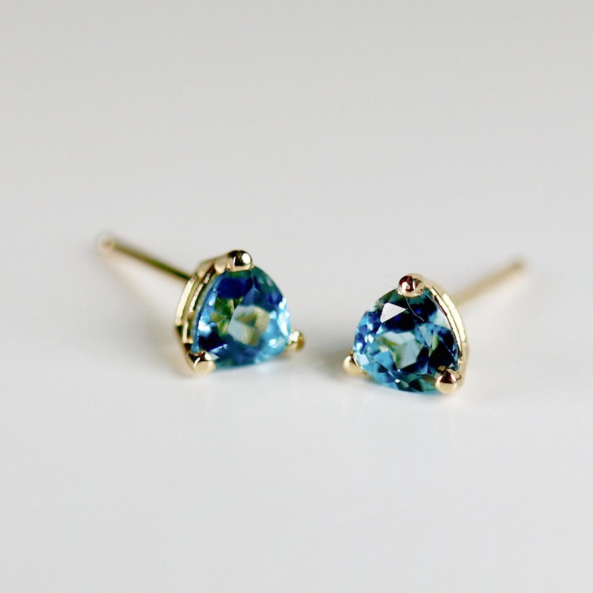 Two blue trillion-cut gemstone stud earrings shown at a slight angle on a neutral background.