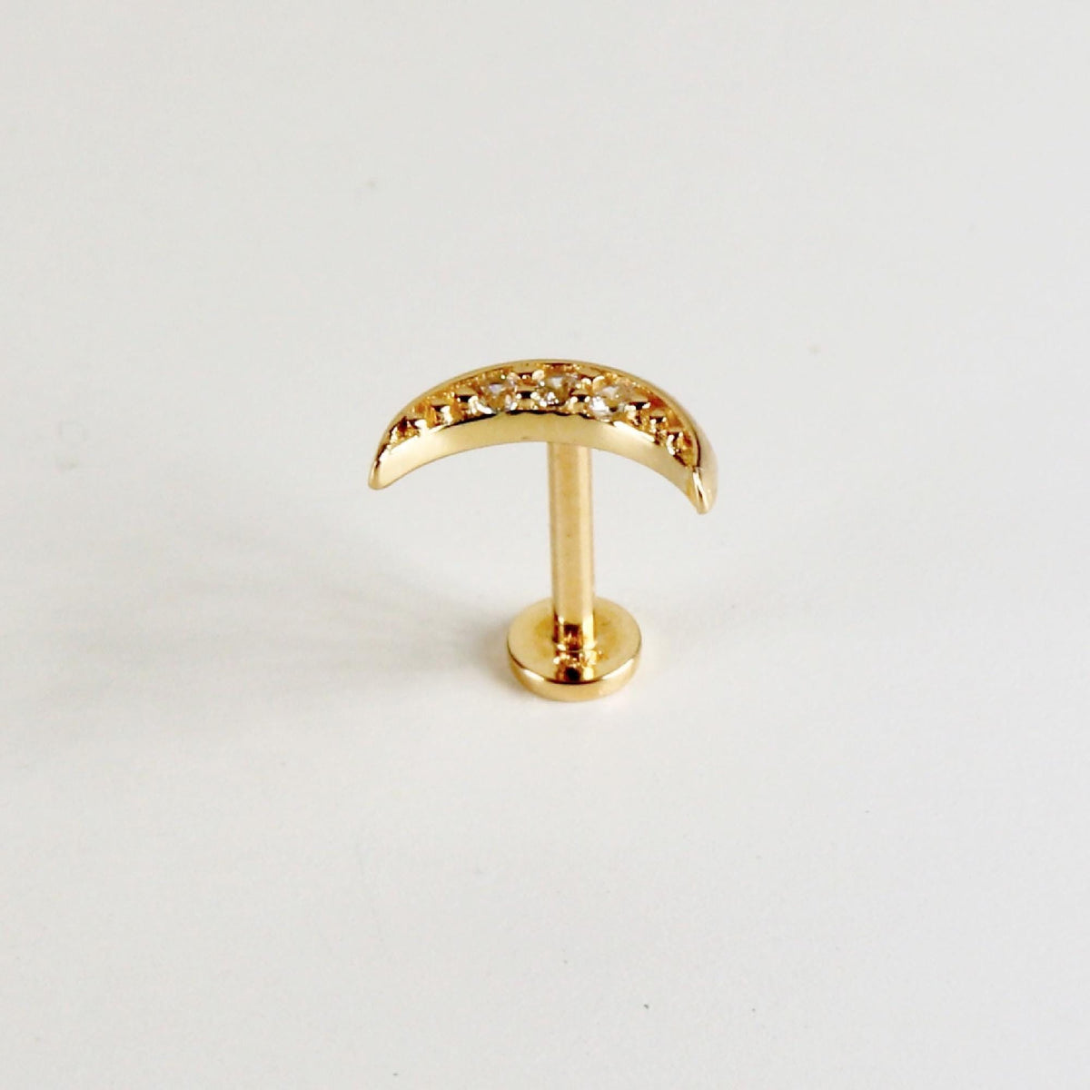 A gold crescent moon flat back earring shown from the base of the post.