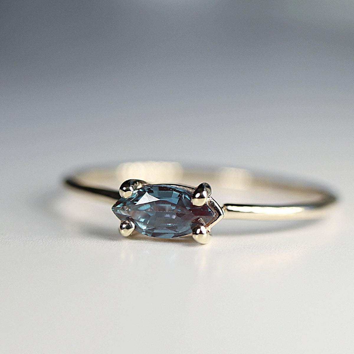 A macro shot of a gold ring featuring a detailed marquise-cut blue and purple stone set horizontally with four prongs.
