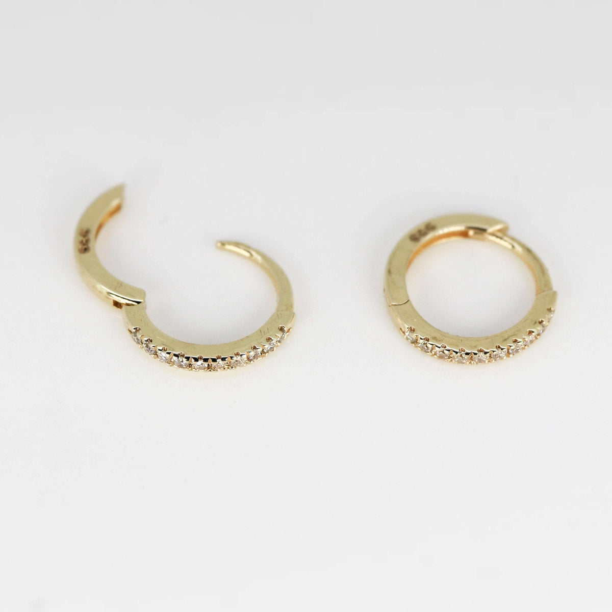 Two gold huggie hoop earrings with pave diamonds, one open and one closed, on a white background.
