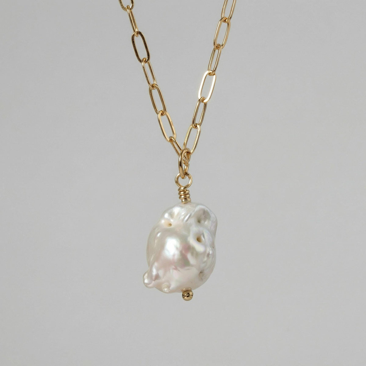 Close-up of a necklace featuring a chunky gold link chain and a single irregular white baroque pearl pendant.