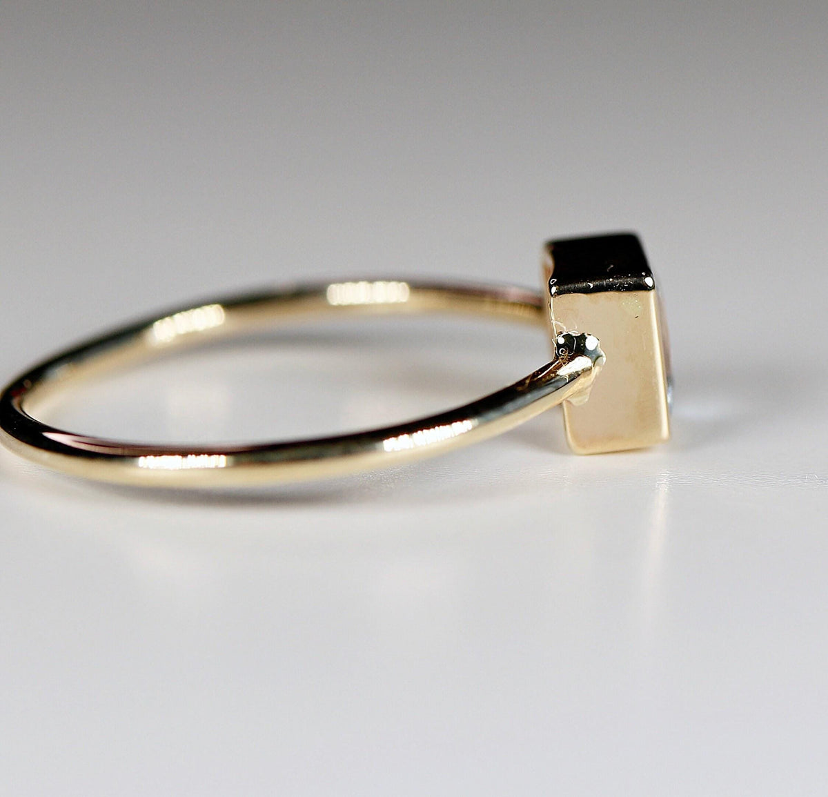 Side profile of a gold ring showing the thick bezel setting of the square gemstone.