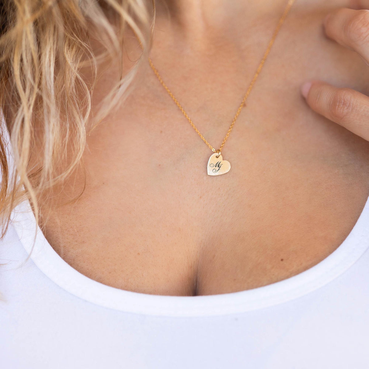A person wearing a gold heart pendant necklace against a white background.