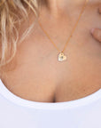 A person wearing a gold heart pendant necklace against a white background.