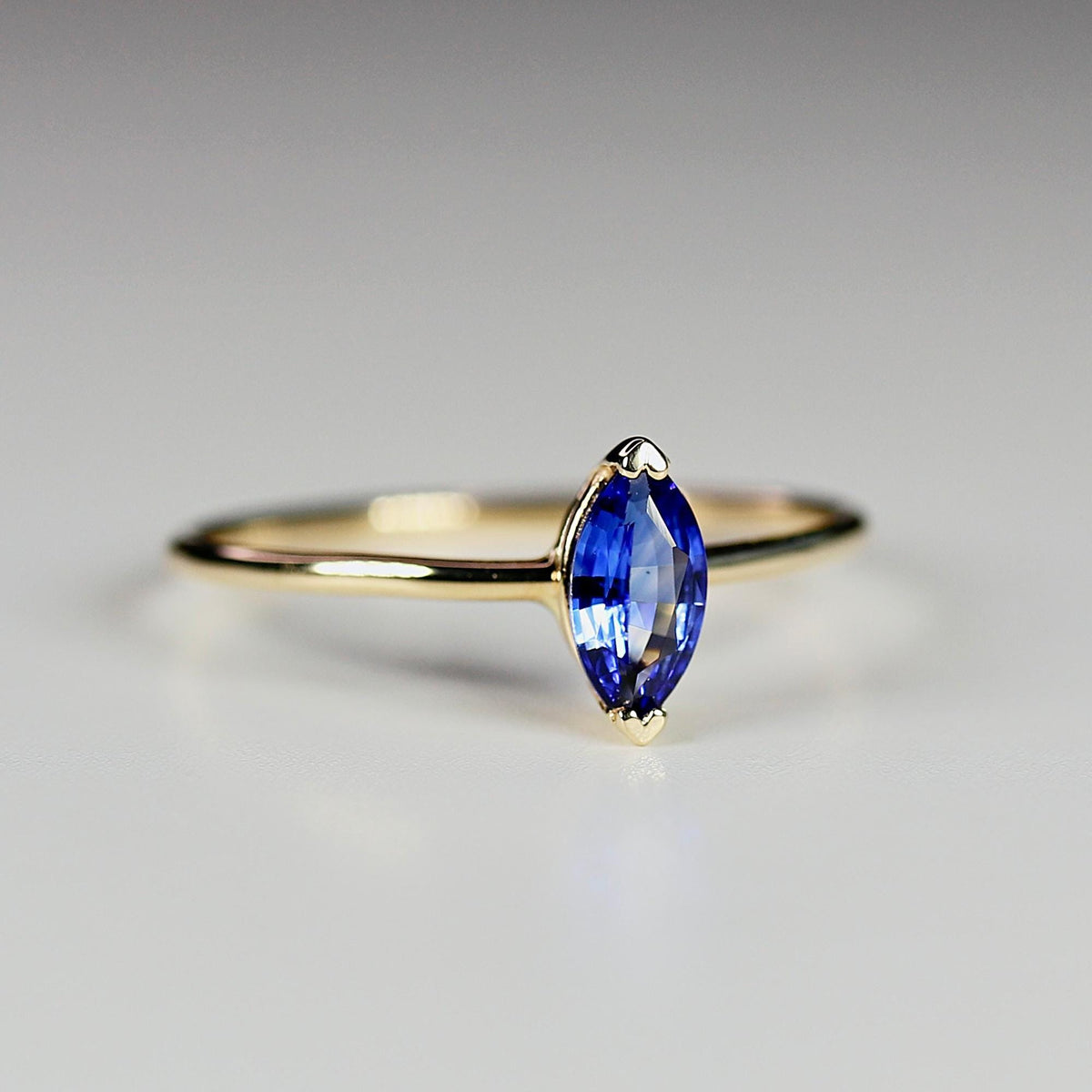 A gold ring with a marquise-cut blue sapphire captured in a slight angle view against a neutral white background.